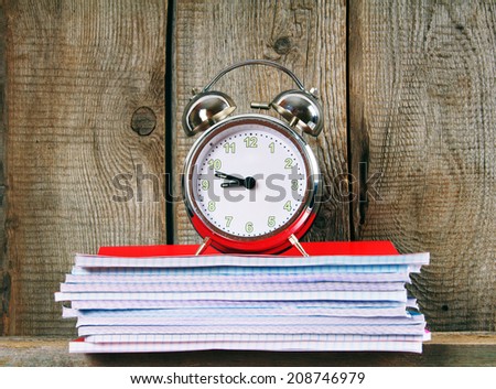 Writing-books and an alarm clock on a wooden shelf. A wooden background.