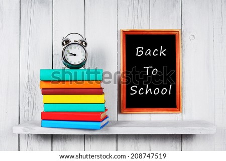 Back to school. Books and an alarm clock on a wooden shelf. A white, wooden background.