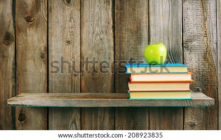 Multi-coloured books and green apple on a wooden shelf. On a wooden background.