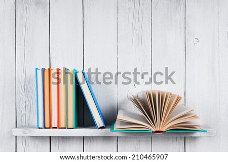 The open book and other multi-coloured books. On a wooden shelf. A wooden, white background.