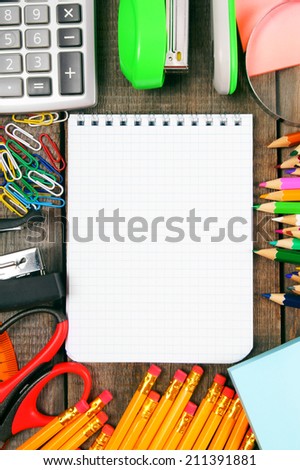 Back to school. A notebook and school tools around. Vertically. A wooden background.