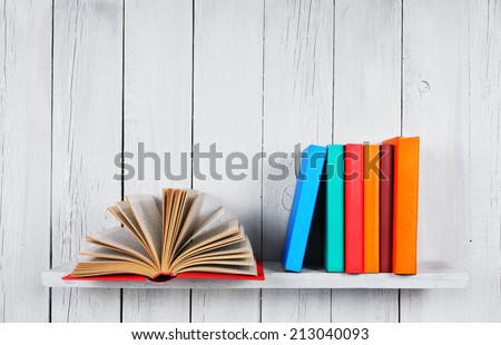 The open book and other multi-coloured books. On a wooden shelf. A wooden, white background.