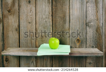 Apple and writing-books on a wooden shelf. On a wooden background.