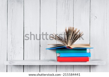 The open book on other multi-coloured books. On a wooden shelf. A wooden, white background.