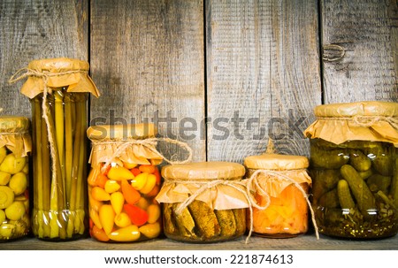 Preserved food in glass jars, on a wooden shelf. Various marinaded food, focus on wood