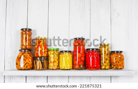 Preserved food in glass jars, on a wooden shelf. Various marinaded food