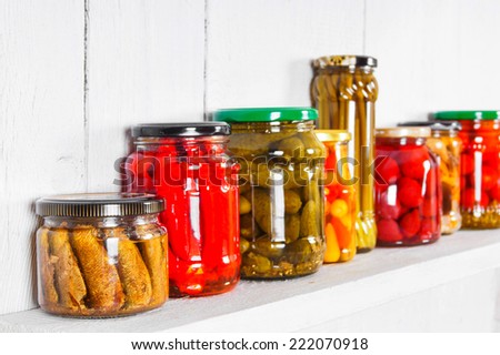 Preserved food in glass jars, on a wooden shelf. Various marinaded food