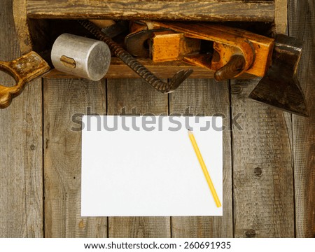 Old working tools. A paper with a pencil and old tools in a box on a wooden background.