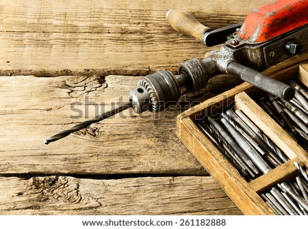 The old working tool. An old drill, a box with drills on a wooden background.