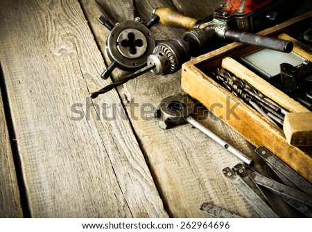 The old working tool. Old drill, a box with drills, pliers and ruler on wooden background.