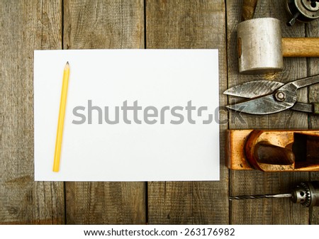 Old working tools. Paper with pencil and the vintage working tools (mallet, emery, scissors and others) on wooden background.