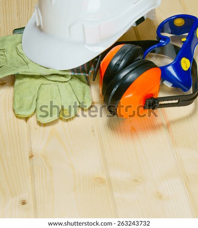 The working tools. A helmet, gloves and ear-phones on a wooden background.