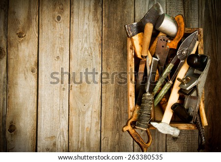 Old working tools. Old working tools (scissors, hammer, chisel and others) in a box on a wooden background.
