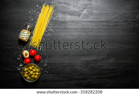 Dry spaghetti with olives, tomatoes and salt. On a black wooden background. Free space for text . Top view