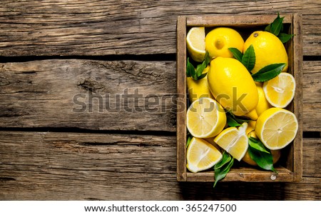 Fresh lemons in an old box with leaves. On wooden background. Free space for text . Top view