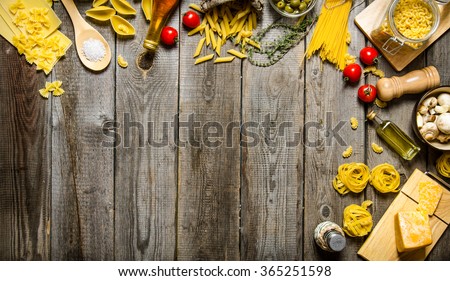 Pasta background. Several types of dry pasta with vegetables, cheese and herbs. On a wooden table.  Free space for text . Top view