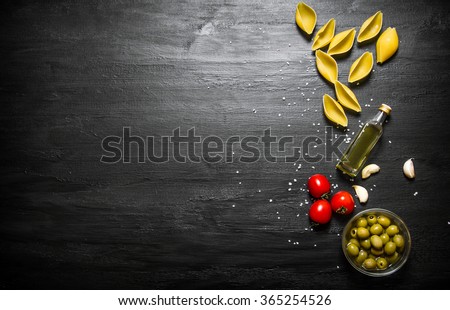 Pasta background. Dry pasta with olive oil and tomatoes. On a black wooden background. Free space for text . Top view