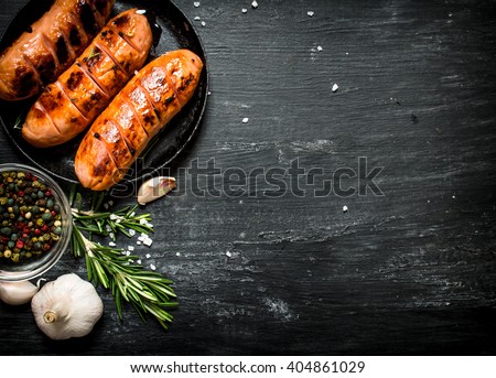 Fried sausages with garlic and herbs in a pan. On the black Board.