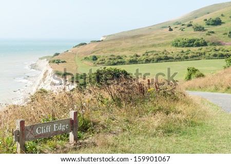 Cliff edge danger sign amongst beautiful scenery on the South Downs Way hiking trail close to Beachy Head and the Seven Sisters, near Eastbourne, England, UK