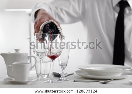 Well dressed man pouring out red wine in an elegant restaurant or hotel dinner table setting