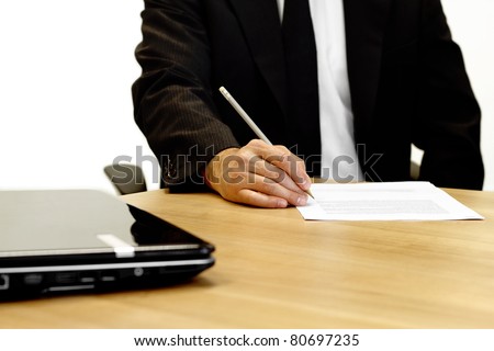 Businessman sitting at a table correcting a document with laptop