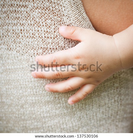 Close-up of baby's hand on the shoulder back of mother