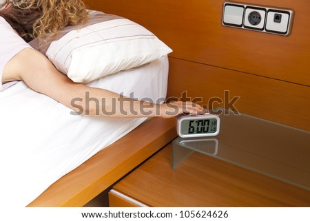 Girl turning off the alarm clock at 6 o\'clock in the morning