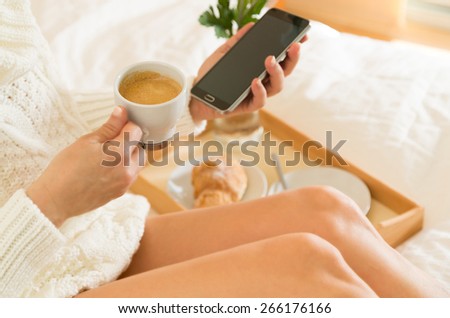 Woman eating breakfast in bed while looking at your mobile phone