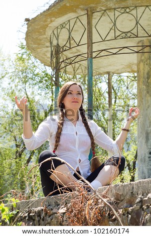 Beautiful woman with long hair meditating near architecture with columns, nature of Almaty at background  / Young woman doing yoga