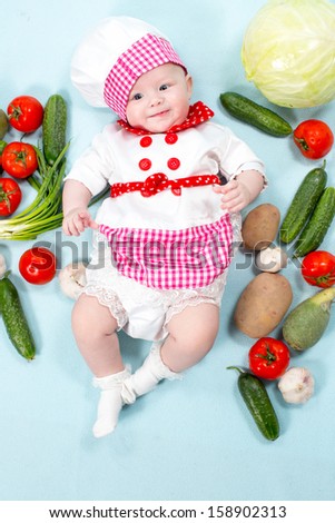 Baby cook girl wearing chef hat with fresh vegetables. Use it for a child, healthy food concept