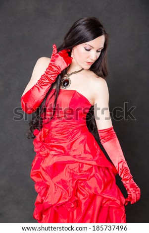 Portrait of beautiful sexy brunette woman with long hair in red satin dress on dark grey background