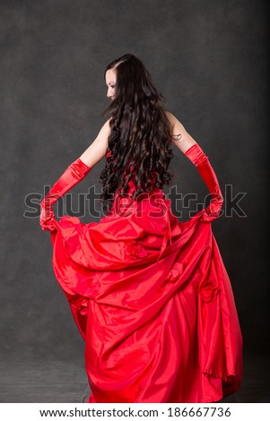 Latino Woman with long hair  in red waving dress dancing  in action with flying fabric on dark grey background