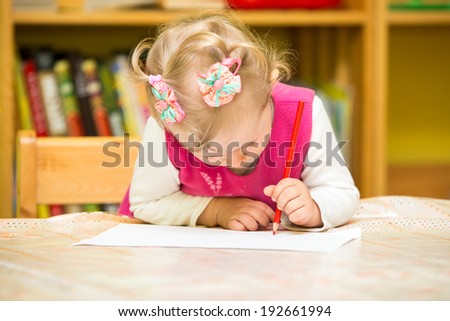 Cute child girl drawing with colorful pencils in preschool at the table in kindergarten