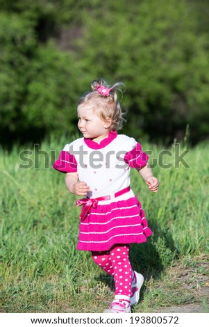 Little child girl  runs on grass on meadow. Summer green nature background