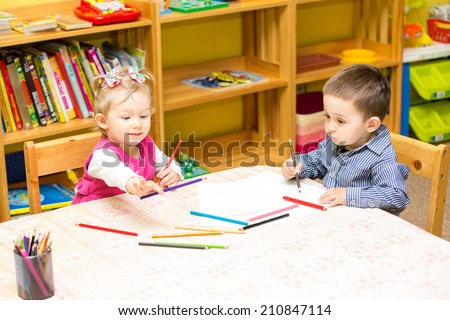 Two little kids drawing with colorful pencils in preschool at the table. Little girl and boy drawing in kindergarten