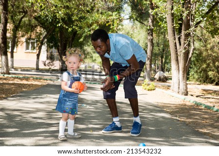 Young African American god father with  little girl playing ball on nature at summer. Use it for baby and sport concept