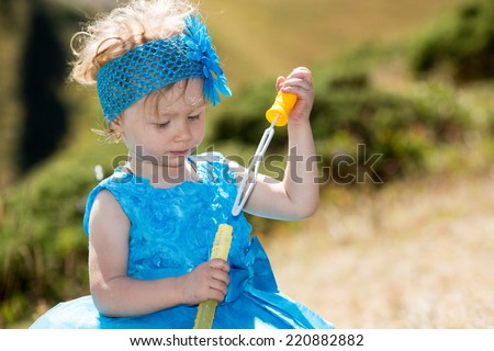 Adorable little child girl with bubble blower on grass on meadow. Summer green nature .  Use it for baby, parenting or love concept