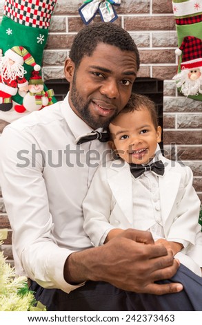 Happy black father and baby boy cuddling by fireplace. Christmas and New Year