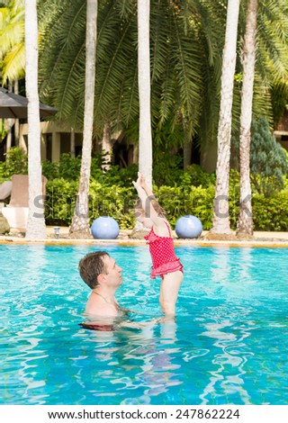 Active father teaching his toddler daughter to swim in pool on tropical resort. Summer vacations and sport  concept
