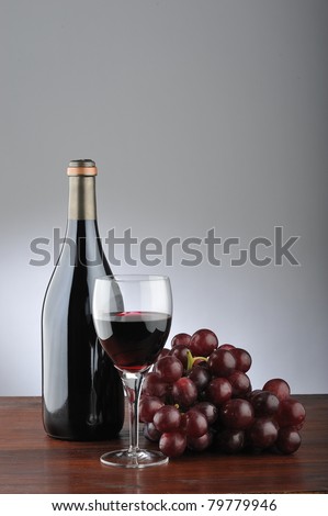 A red wineglass with grapes, bottle and cork