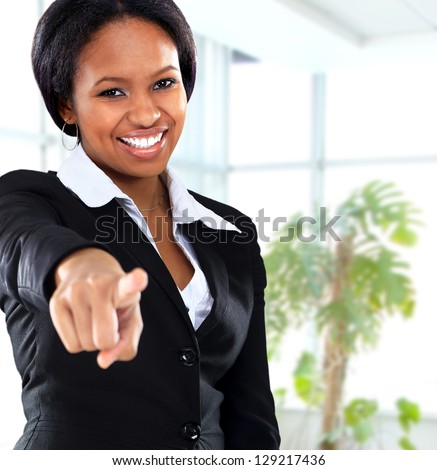 Smiling black business woman pointing on camera in office