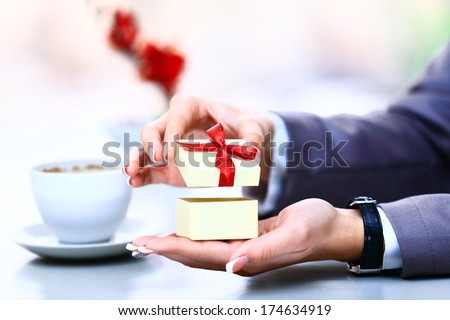 Gift box / present or valentine gift hand close up. Decorative gift box tied with a turquoise ribbon and bow carefully cupped in female hand as she gives a surprise present to a loved one