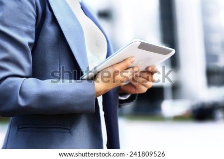 Successful businesswoman or entrepreneur using a digital tablet computer, standing in front of her office.