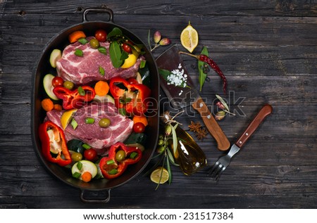 Raw fresh meat with slices of vegetables in a saucepan and meat cleaver with fork on dark background