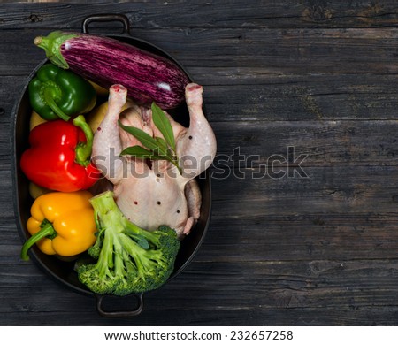 Uncooked chicken with vegetables in a black casserole on a old rustic wooden table with copy-space, top view.