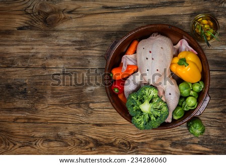uncooked chicken with vegetables in a po ton a old rustic wooden table with copy-space, top view