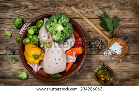 uncooked chicken with vegetables in a pan on a old rustic wooden table, top view
