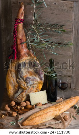 Cured ham leg, cheese, walnuts, bread and bottle of red wine  on a wooden old  background