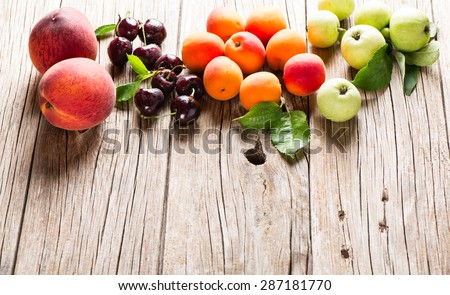 Summer fruits (apples, cherries, apricots, and peaches) with leaves on a old wooden  background