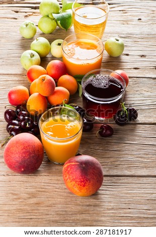 Summer fruits and juices (apples, cherries, apricots, and peaches) on a old wooden background. Selective focus is on the glass of cherry juice.